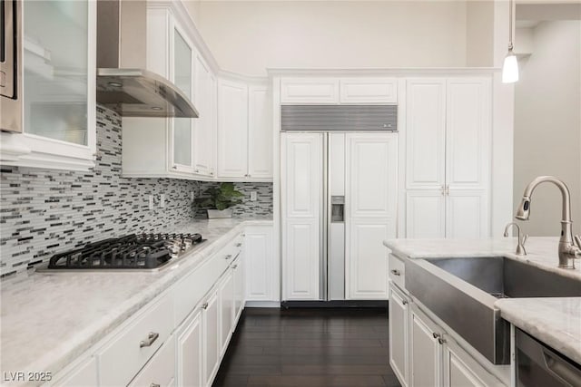 kitchen with appliances with stainless steel finishes, white cabinets, hanging light fixtures, and wall chimney exhaust hood