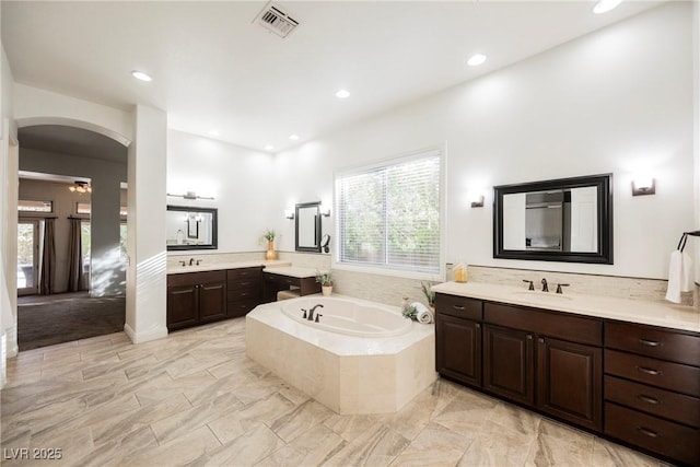 bathroom with a bath, two vanities, a sink, and recessed lighting