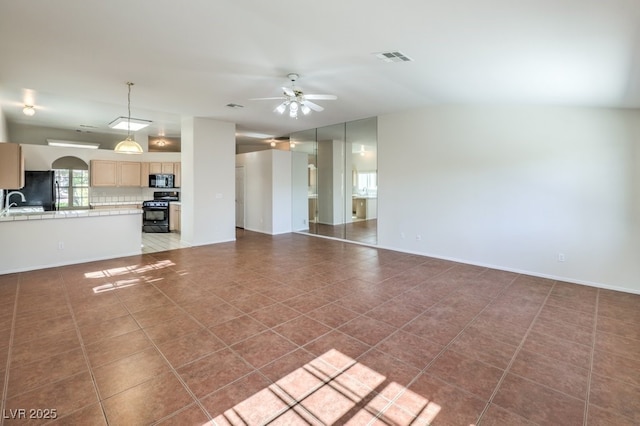 unfurnished living room with dark tile patterned floors, a sink, visible vents, a ceiling fan, and baseboards