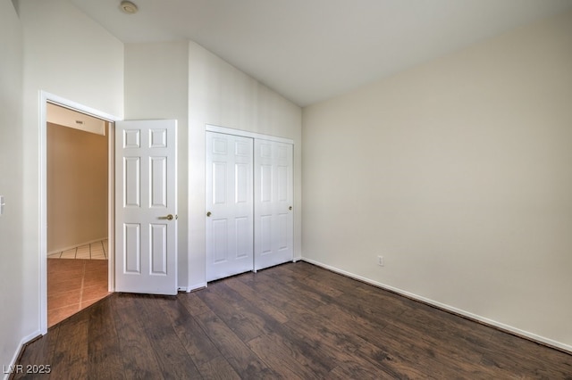 unfurnished bedroom with dark wood-style floors, baseboards, vaulted ceiling, and a closet