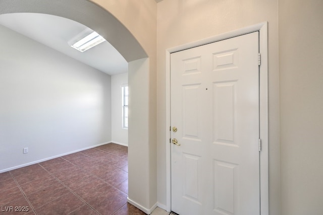 foyer entrance with dark tile patterned floors, arched walkways, vaulted ceiling, and baseboards