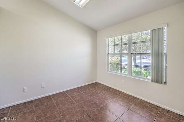 unfurnished room with lofted ceiling, dark tile patterned floors, and baseboards