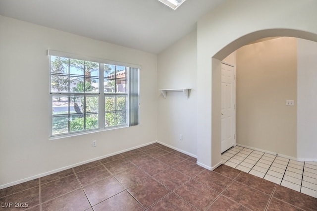 empty room featuring lofted ceiling, arched walkways, dark tile patterned floors, and baseboards