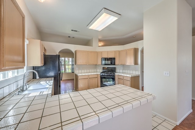 kitchen featuring arched walkways, tile counters, visible vents, light brown cabinetry, and black appliances