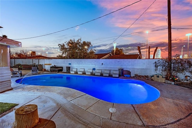 pool at dusk with a patio area, a fenced backyard, and a fenced in pool