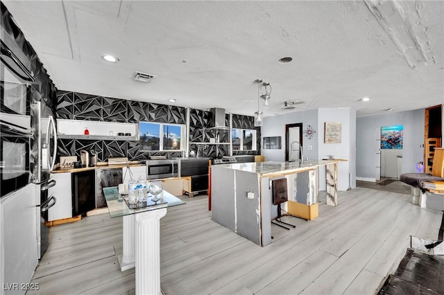 kitchen featuring pendant lighting, stainless steel microwave, a kitchen island with sink, light wood-type flooring, and a kitchen bar