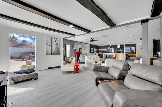 living area featuring ceiling fan, light wood finished floors, visible vents, and beam ceiling