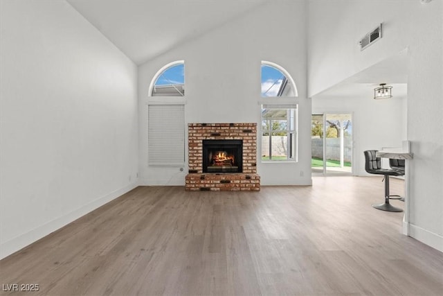 unfurnished living room featuring visible vents, high vaulted ceiling, wood finished floors, a fireplace, and baseboards