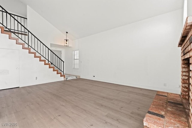 unfurnished living room with a brick fireplace, high vaulted ceiling, stairs, and wood finished floors