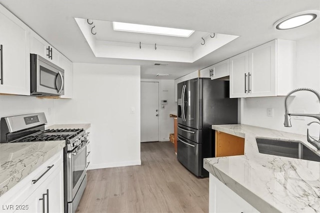 kitchen featuring a sink, a tray ceiling, white cabinetry, light wood-style floors, and appliances with stainless steel finishes