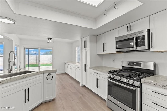 kitchen with a sink, light wood-style floors, white cabinetry, and stainless steel appliances