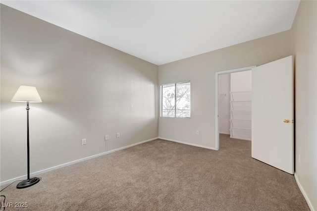 unfurnished bedroom featuring a walk in closet, light colored carpet, and baseboards