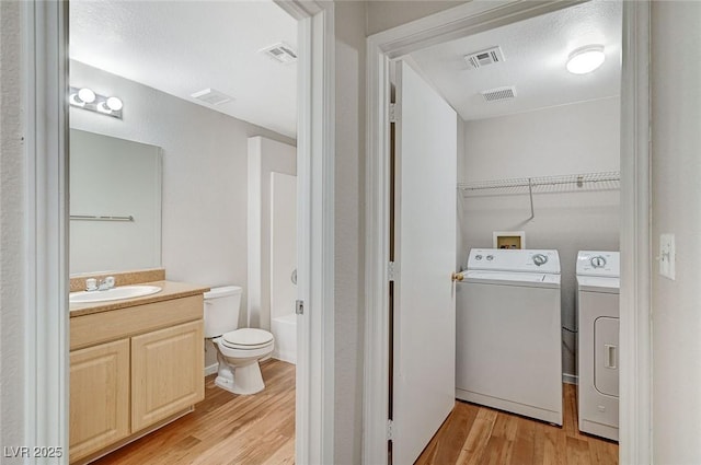 full bathroom featuring visible vents, independent washer and dryer, vanity, and wood finished floors