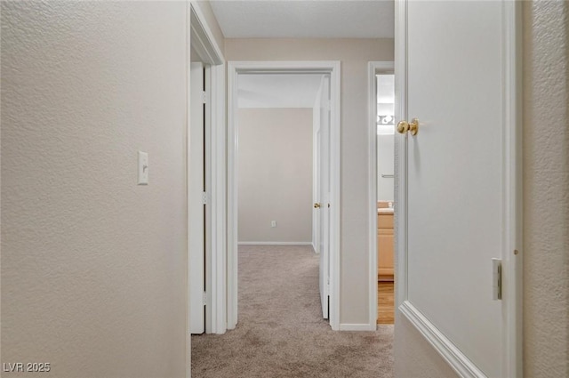 hallway with a textured wall, baseboards, and light colored carpet