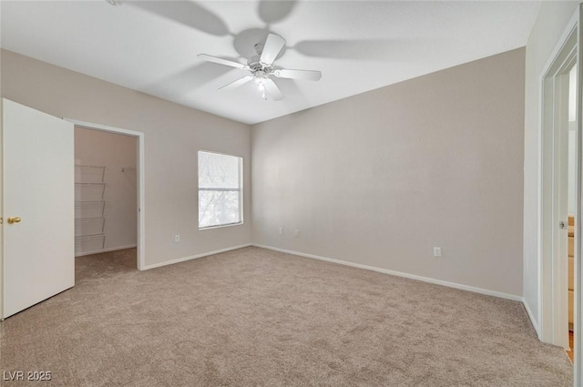 unfurnished bedroom featuring light carpet, a spacious closet, and baseboards