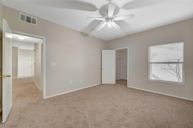 unfurnished bedroom featuring a walk in closet, light colored carpet, visible vents, ceiling fan, and baseboards