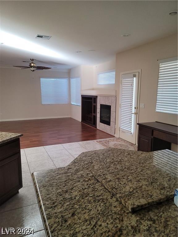 living area featuring visible vents, baseboards, a tile fireplace, ceiling fan, and light tile patterned flooring