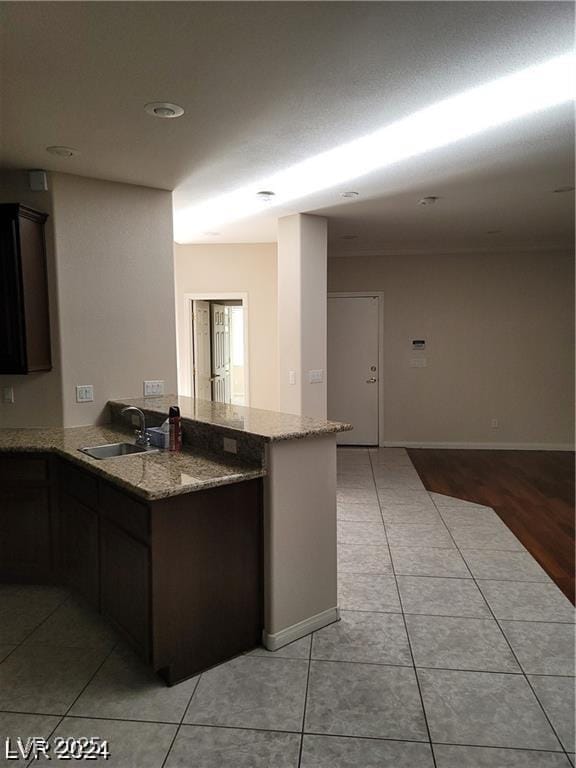 kitchen with light tile patterned floors, light stone counters, a peninsula, a sink, and dark brown cabinets