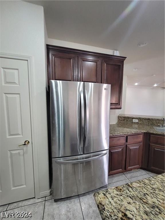 kitchen with dark stone counters, light tile patterned flooring, a sink, and freestanding refrigerator