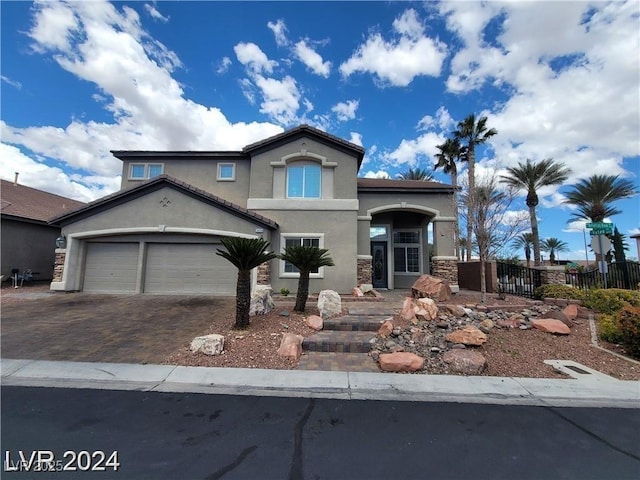 mediterranean / spanish-style house featuring a garage, fence, stone siding, decorative driveway, and stucco siding