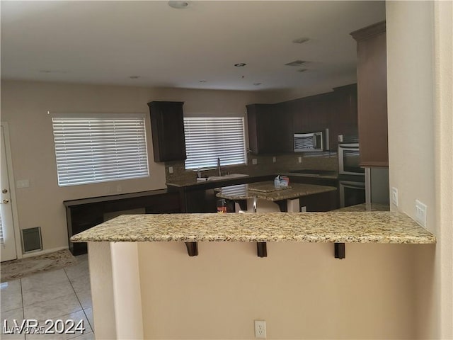 kitchen featuring light tile patterned floors, a peninsula, a breakfast bar area, and a sink