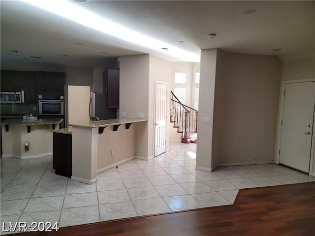 kitchen featuring light tile patterned floors, appliances with stainless steel finishes, light stone counters, and a kitchen breakfast bar