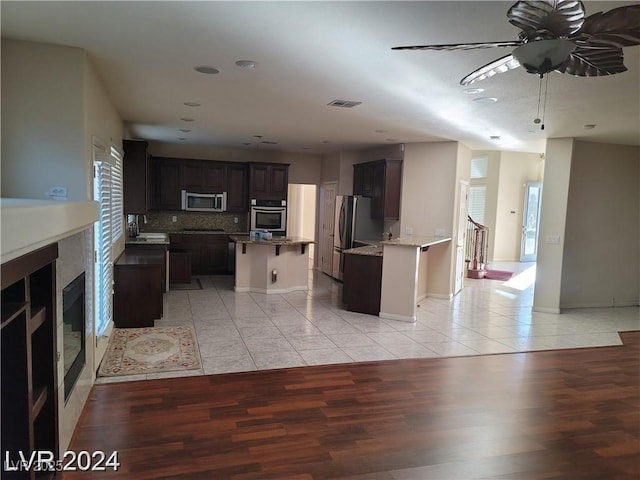 kitchen featuring light tile patterned flooring, stainless steel appliances, visible vents, dark brown cabinets, and a center island