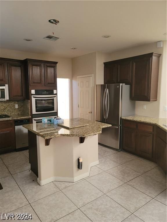 kitchen featuring stainless steel appliances, a kitchen island, visible vents, a kitchen breakfast bar, and light stone countertops