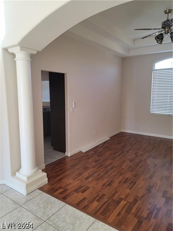 empty room with ornate columns, ceiling fan, baseboards, and light wood finished floors