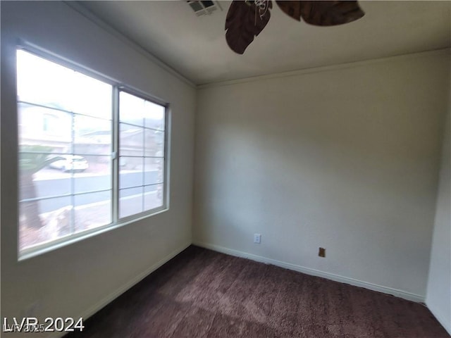 empty room with visible vents, ceiling fan, dark carpet, and a wealth of natural light