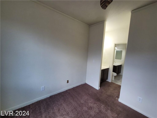 unfurnished bedroom with connected bathroom, dark carpet, and baseboards