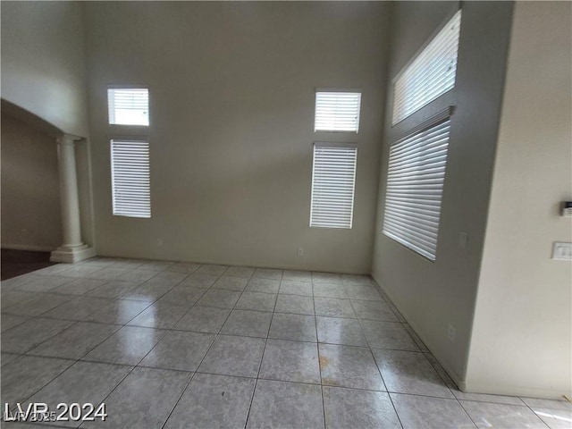 unfurnished room featuring light tile patterned floors, a healthy amount of sunlight, a towering ceiling, and ornate columns