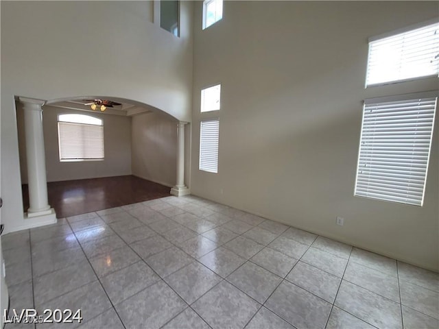 unfurnished room featuring arched walkways, light tile patterned flooring, ceiling fan, and ornate columns