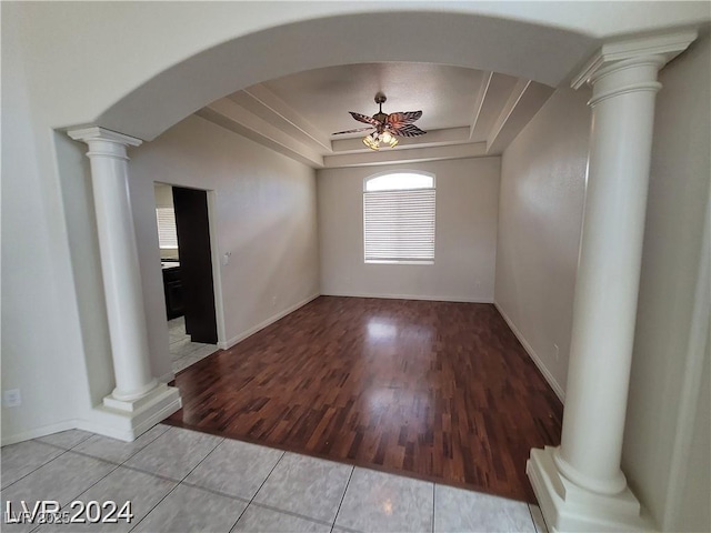 empty room with arched walkways, ceiling fan, light wood-type flooring, a raised ceiling, and ornate columns