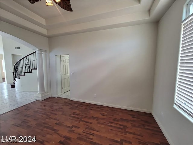 empty room featuring arched walkways, a raised ceiling, visible vents, ornate columns, and stairs