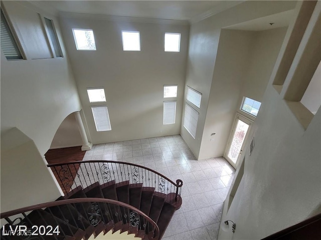 stairway featuring arched walkways, visible vents, a towering ceiling, ornamental molding, and tile patterned flooring