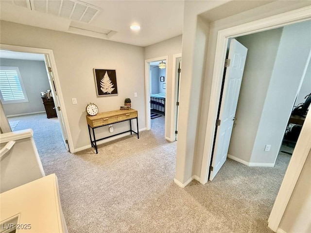 corridor with light colored carpet, visible vents, and baseboards