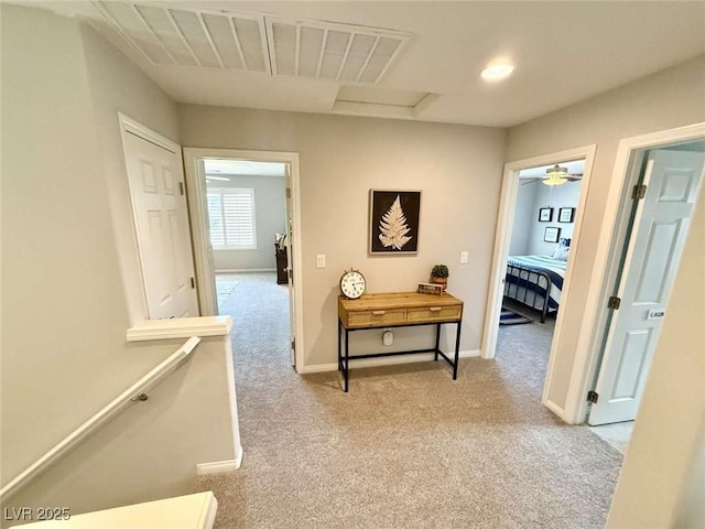 corridor with light carpet, visible vents, an upstairs landing, and baseboards