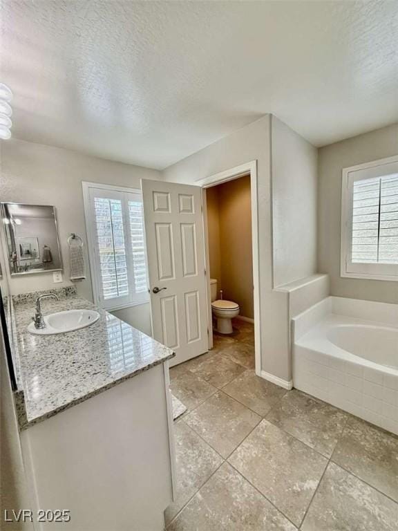 bathroom featuring toilet, vanity, a textured ceiling, baseboards, and a bath