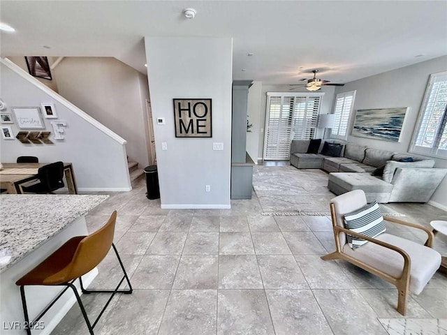 living room featuring a ceiling fan, light tile patterned flooring, stairway, and baseboards