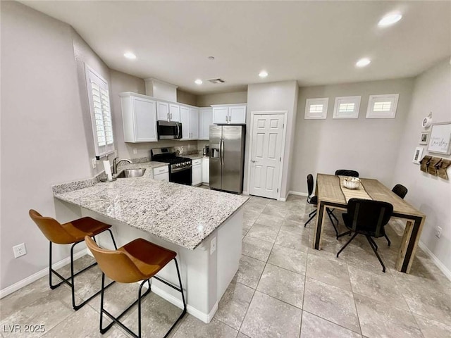 kitchen featuring light stone counters, a peninsula, a sink, white cabinets, and appliances with stainless steel finishes