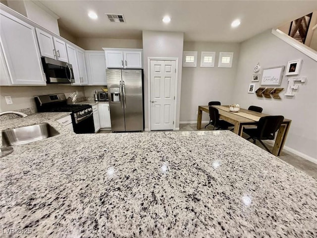 kitchen with stainless steel appliances, light stone counters, a sink, and white cabinetry