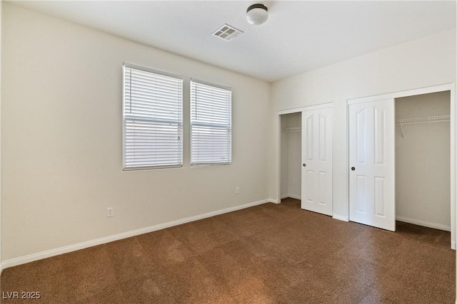 unfurnished bedroom with baseboards, visible vents, dark carpet, and two closets