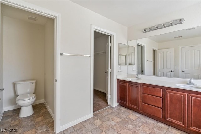 bathroom featuring toilet, double vanity, a sink, and visible vents