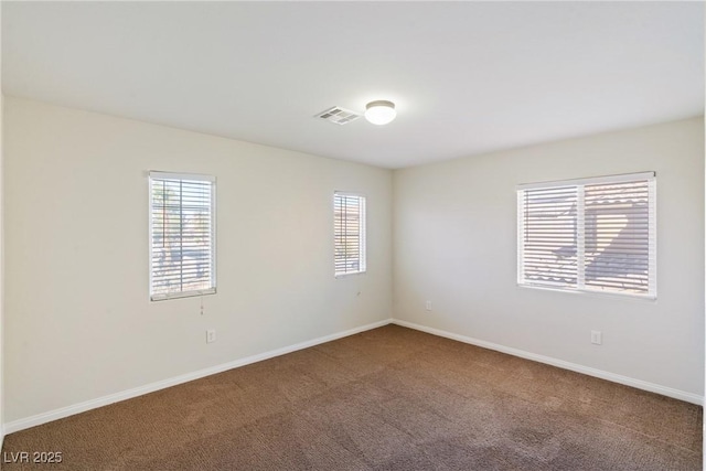 empty room with a wealth of natural light, carpet, visible vents, and baseboards