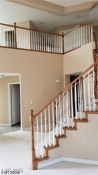 staircase featuring carpet floors, a towering ceiling, and baseboards