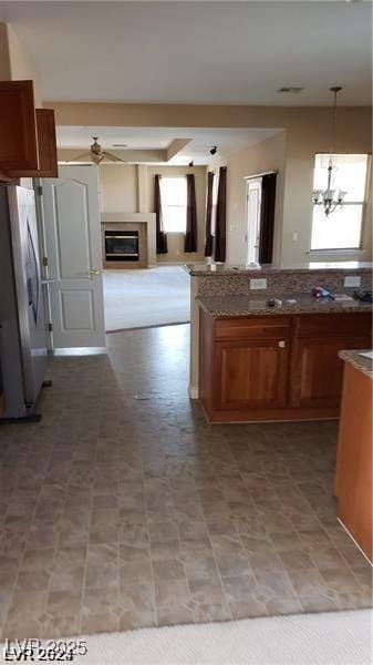 kitchen with open floor plan, freestanding refrigerator, brown cabinets, a glass covered fireplace, and decorative light fixtures