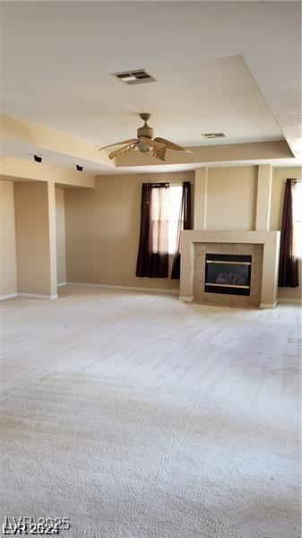 unfurnished living room with carpet, a tray ceiling, visible vents, a tiled fireplace, and ceiling fan