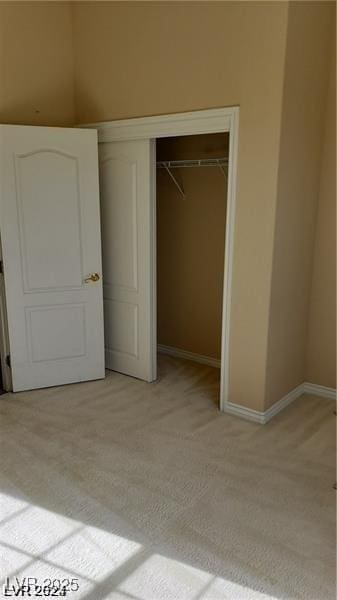 unfurnished bedroom featuring baseboards, a closet, and light colored carpet