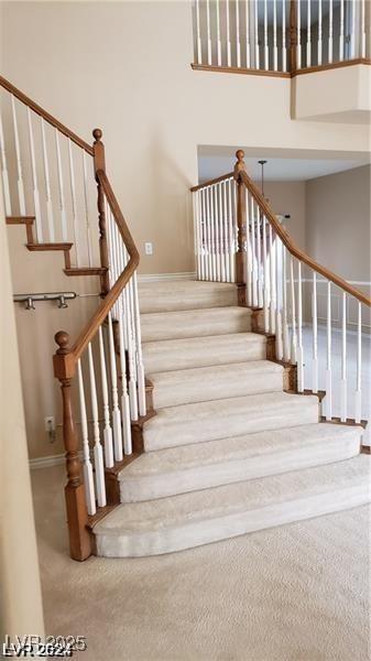 staircase featuring carpet, a towering ceiling, and baseboards